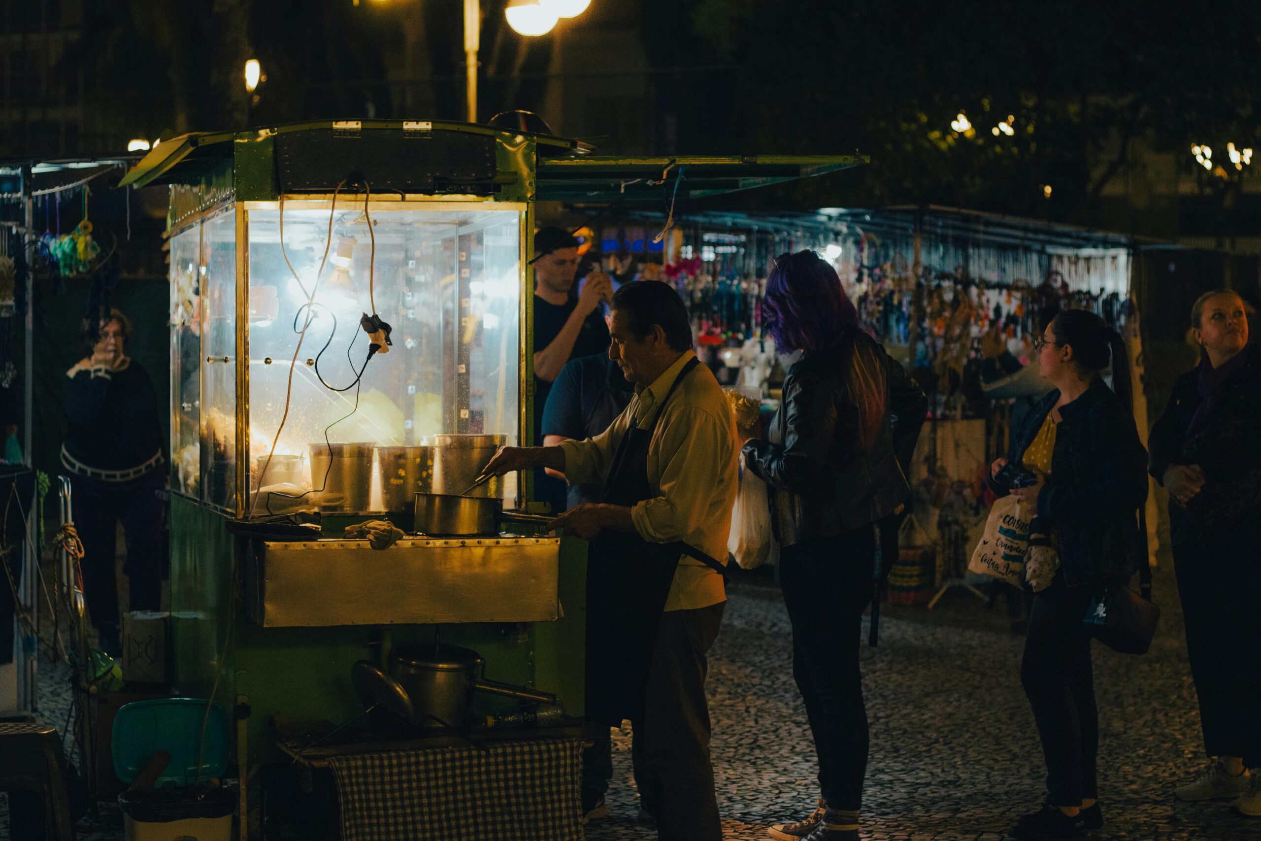 GeschÃ¤ftiges StraÃŸenbild auf dem Nachtmarkt mit LebensmittelverkÃ¤ufern und Kunden an den StraÃŸenstÃ¤nden.