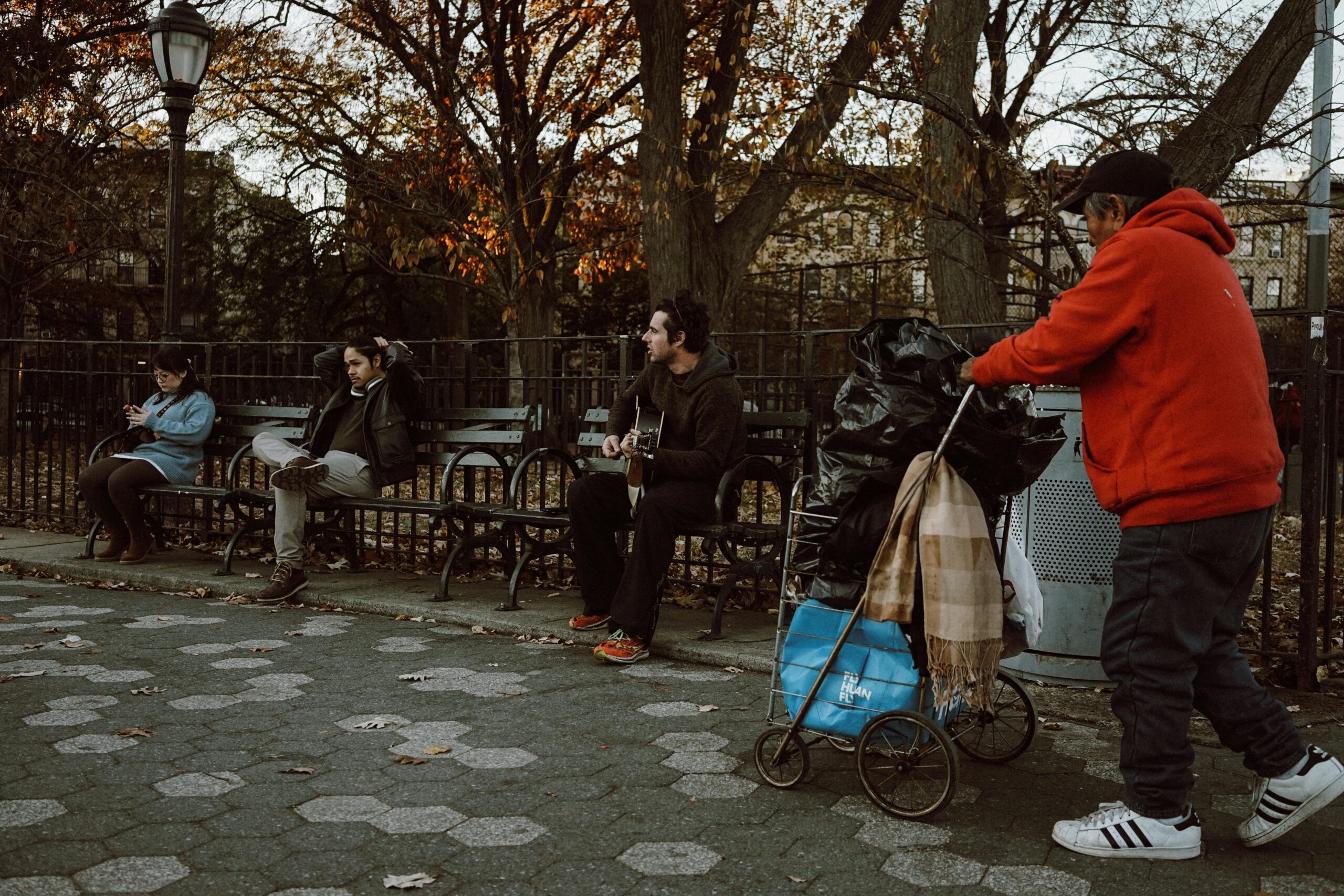 Ein StraÃŸenmusiker spielt in einem Park Gitarre, wÃ¤hrend Menschen vorbeigehen, und fÃ¤ngt so die Essenz des stÃ¤dtischen Lebens ein.