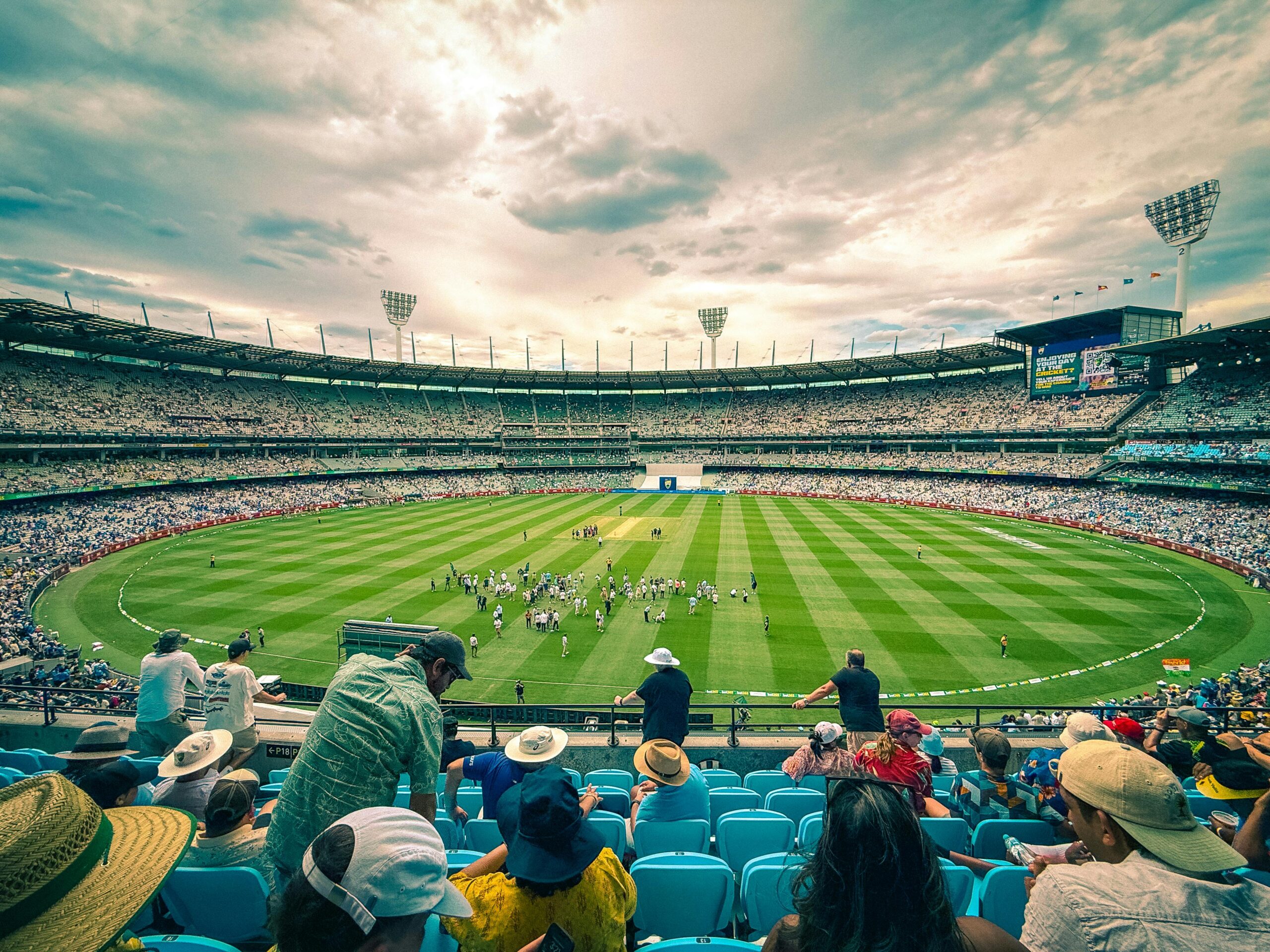 Ein spannendes Cricket-Match im Melbourne Cricket Ground mit einer bunten Menschenmenge unter einem dynamischen Himmel.