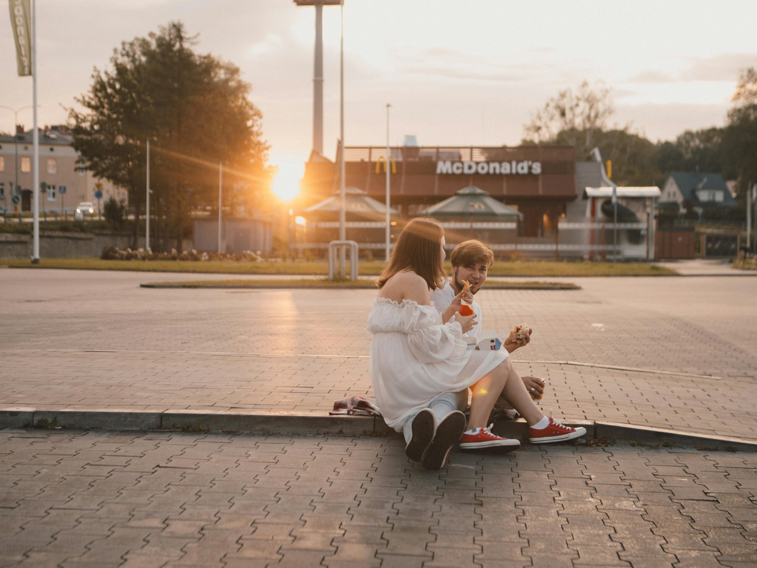 Zwei Teenager sitzen bei Sonnenuntergang drauÃŸen in der NÃ¤he von McDonald's und genieÃŸen ein Eis.