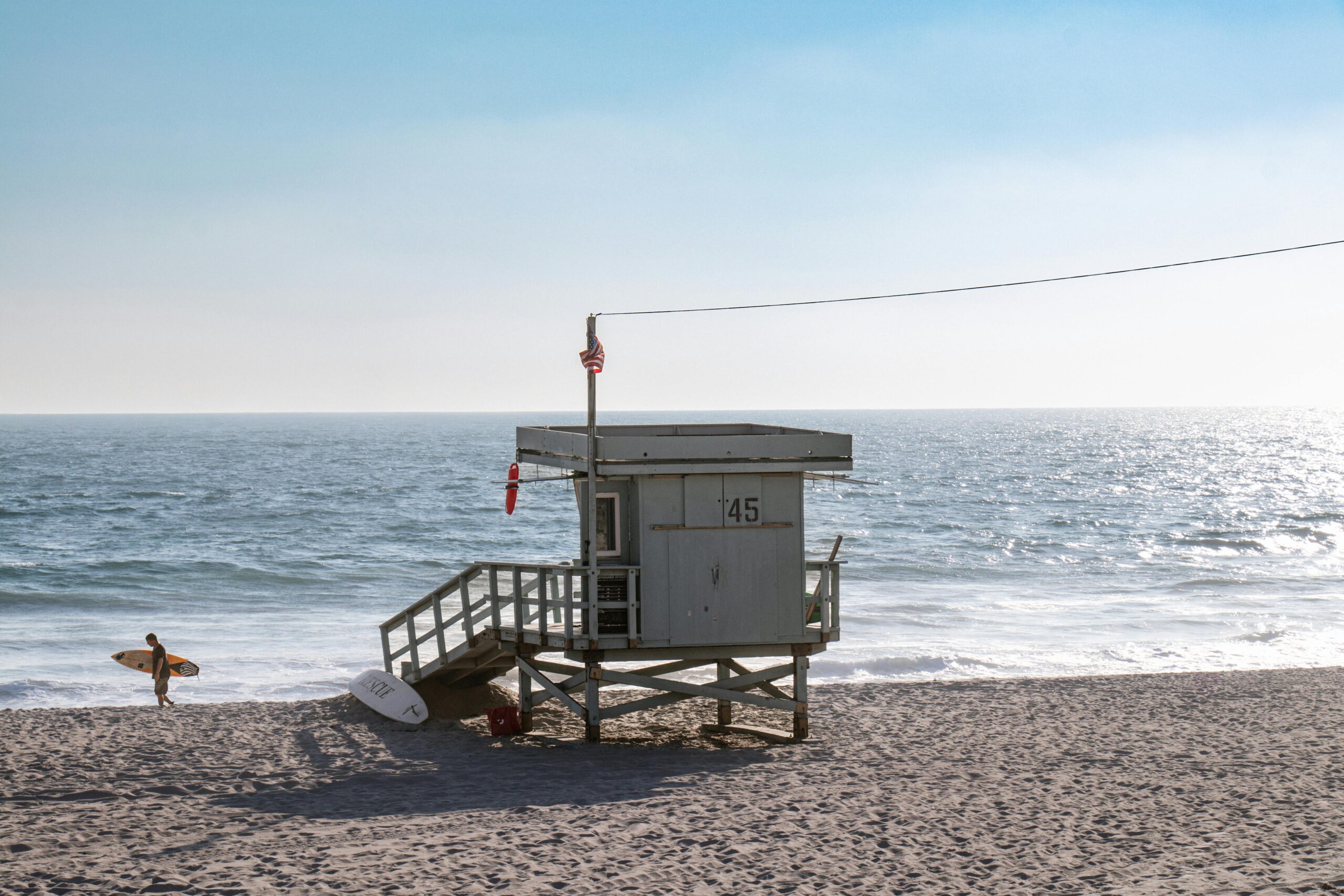 Eine malerische Aussicht auf einen Rettungsschwimmerturm an einem sonnigen Strand in Kalifornien mit einem Surfer in der NÃ¤he.