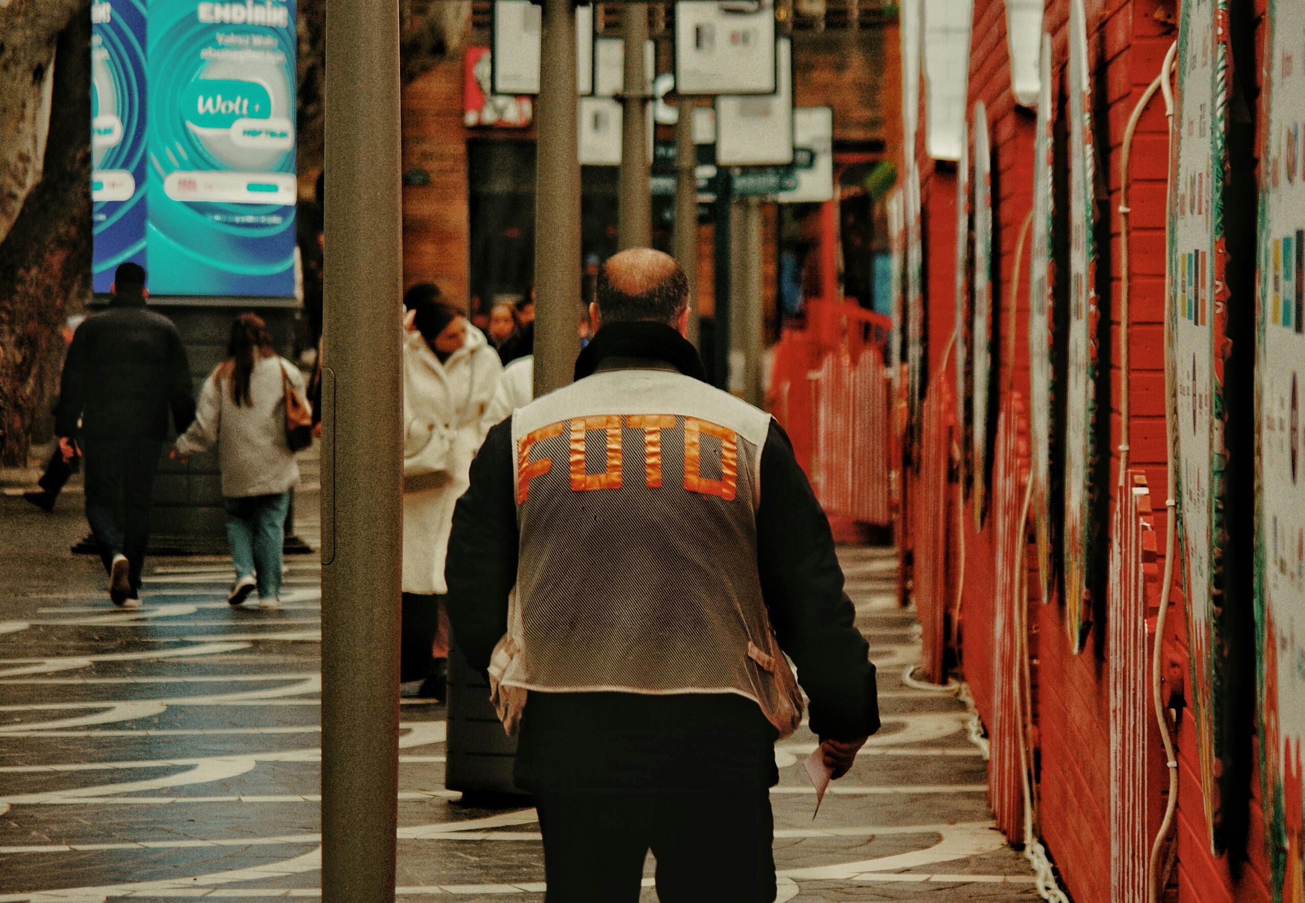 Belebte stÃ¤dtische StraÃŸenszene mit Passanten und einem Mann in einer FOTO-Jacke.